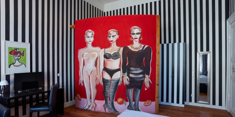 Ein cooles Hotelzimmer in schwarz-weiß gestreift und mit drei gemalten Frauen an der Wand.